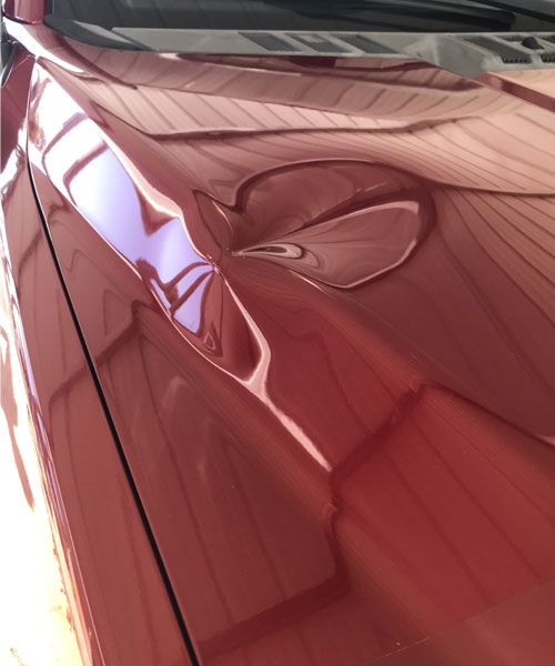 car-paint-scratch-body-dent-repair-near-me-dentsville-sc Dent visible on red vehicle hood before repair.