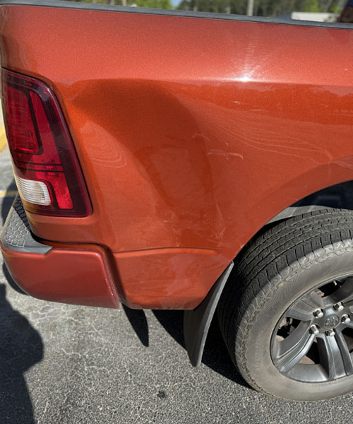 White sports car fender with large dent and rusted scrape above the wheel.