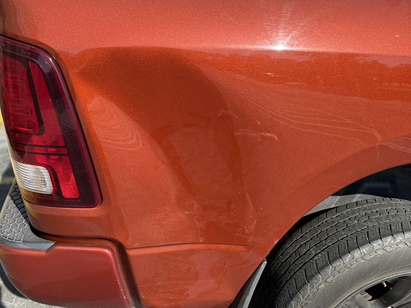 White sports car fender with large dent and rusted scrape above the wheel.